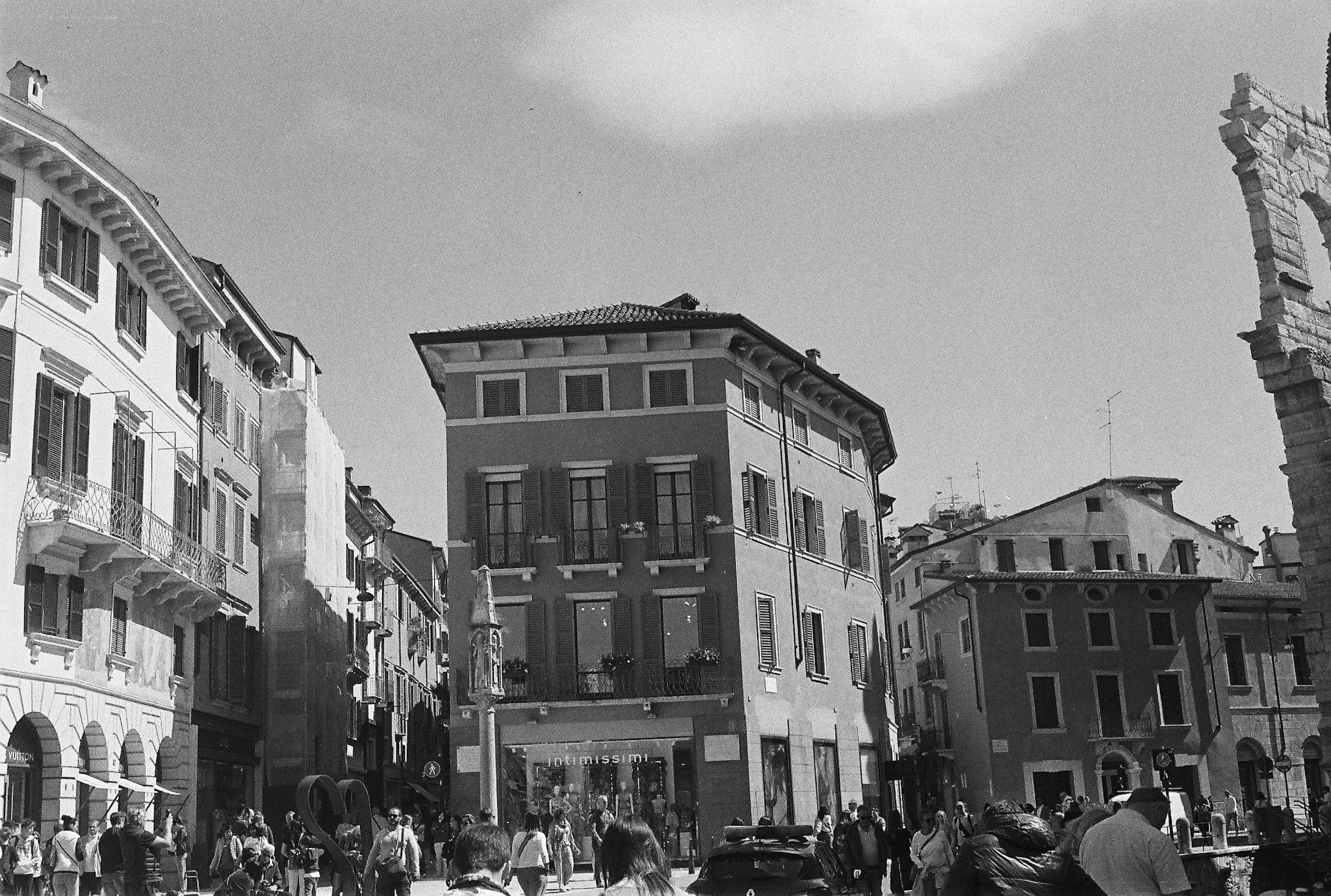 Black-and-white busy shopping scene in Verona with Intimissimi signage, partial Vuitton sign and historic buildings.
