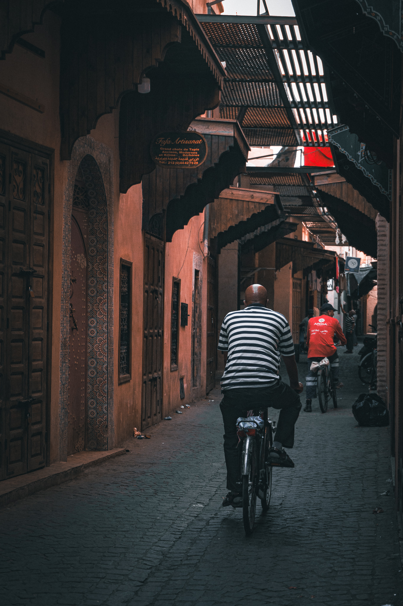 Cyclists moving through a shaded souk lane with striped light in Marrakech