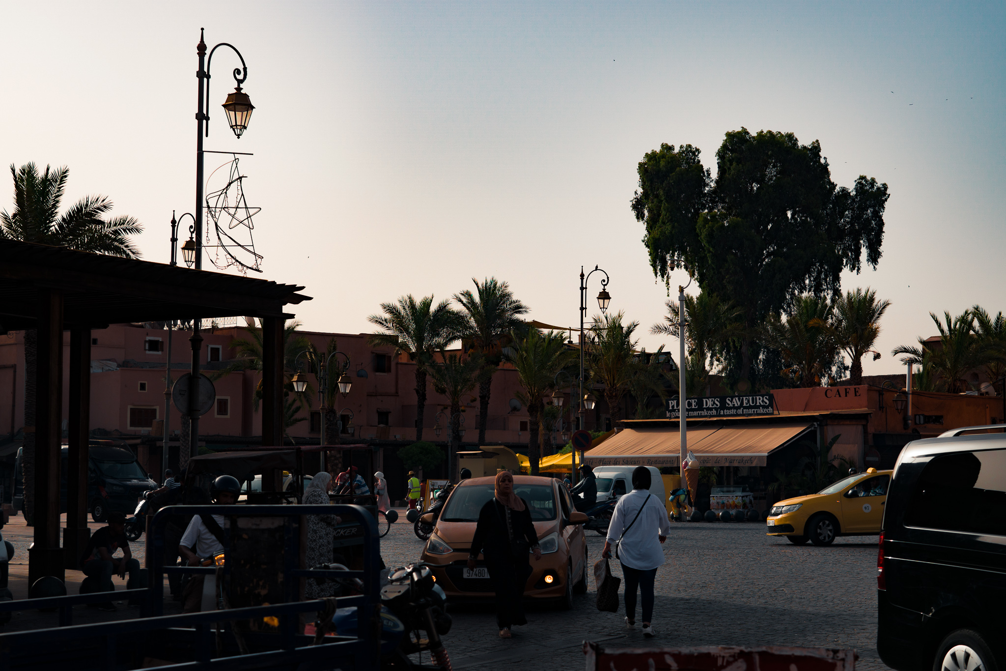 Plaza scene in Marrakech with taxis, kiosks, palm trees, and pedestrians
