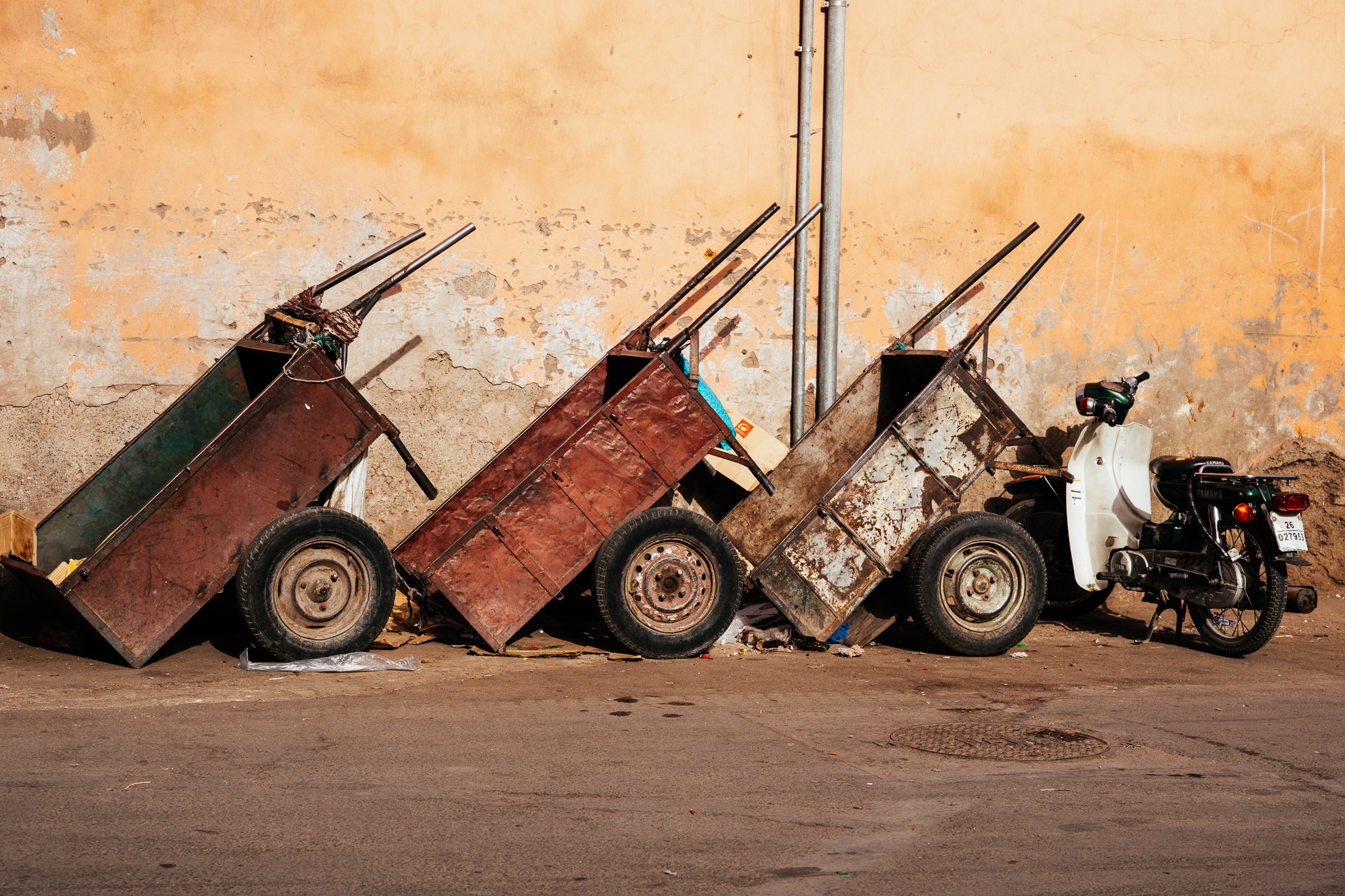 Metal utility carts and a scooter against a weathered wall in Marrakech