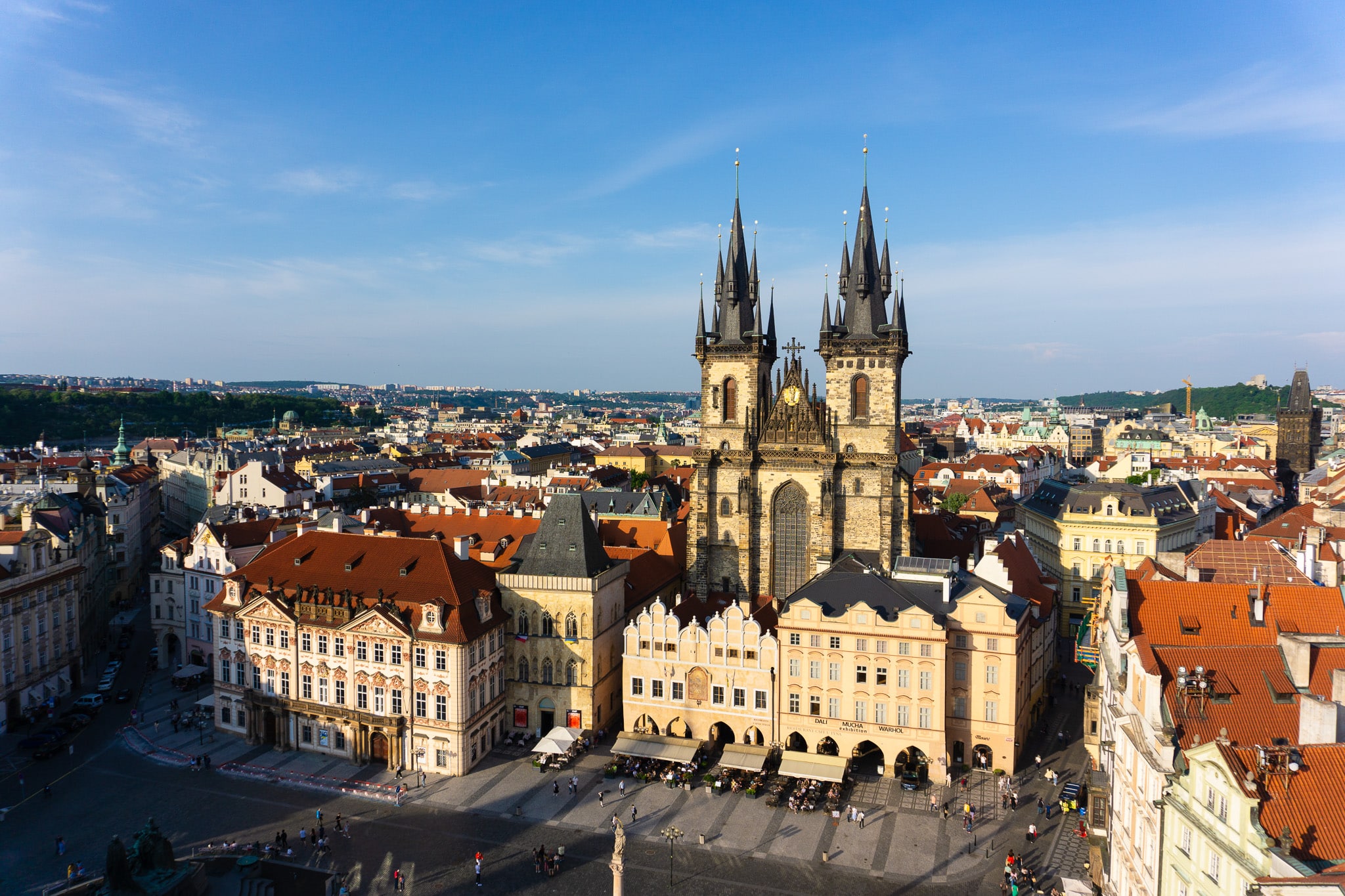 Elevated view over Prague Old Town with Týn Church and signs for Dali, Mucha, and Warhol exhibitions.