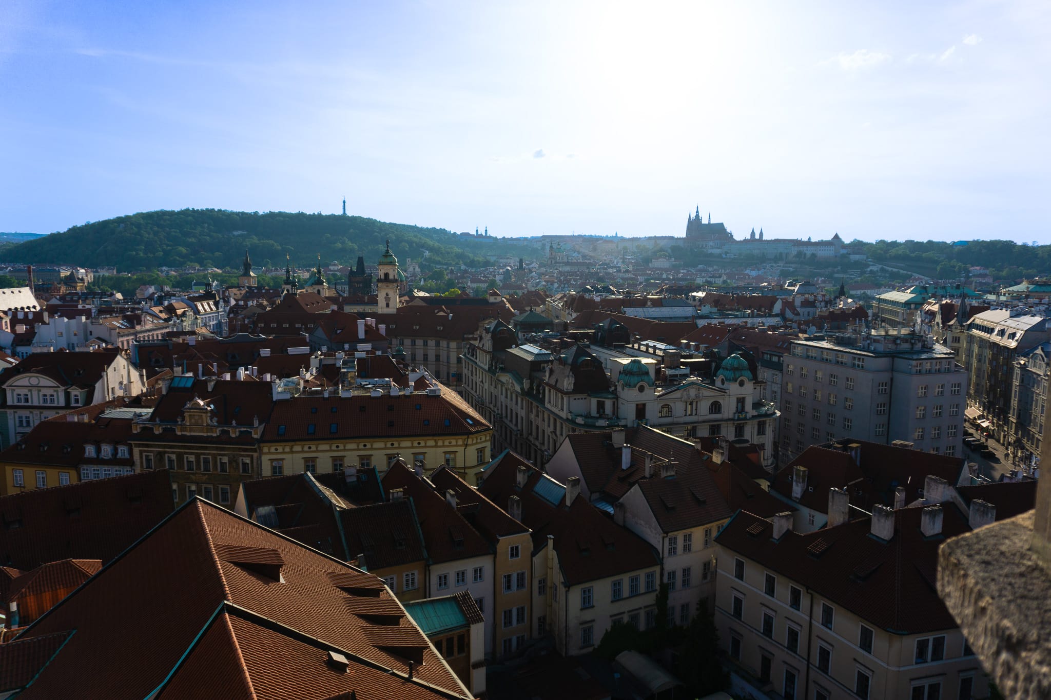 Panoramic view over Prague rooftops with church towers and hilltop landmarks.
