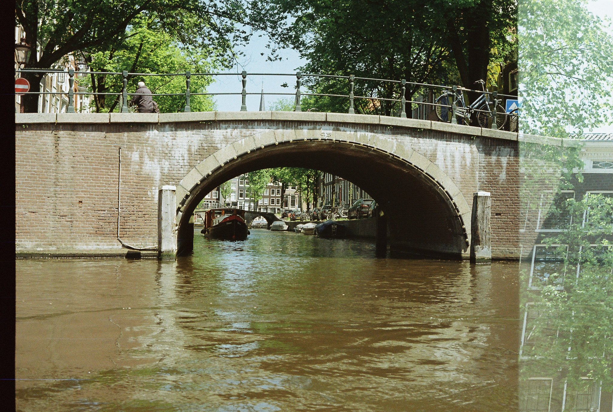 Brick arched bridge over an Amsterdam canal with a parked bicycle, pedestrian, and boats visible through the arch