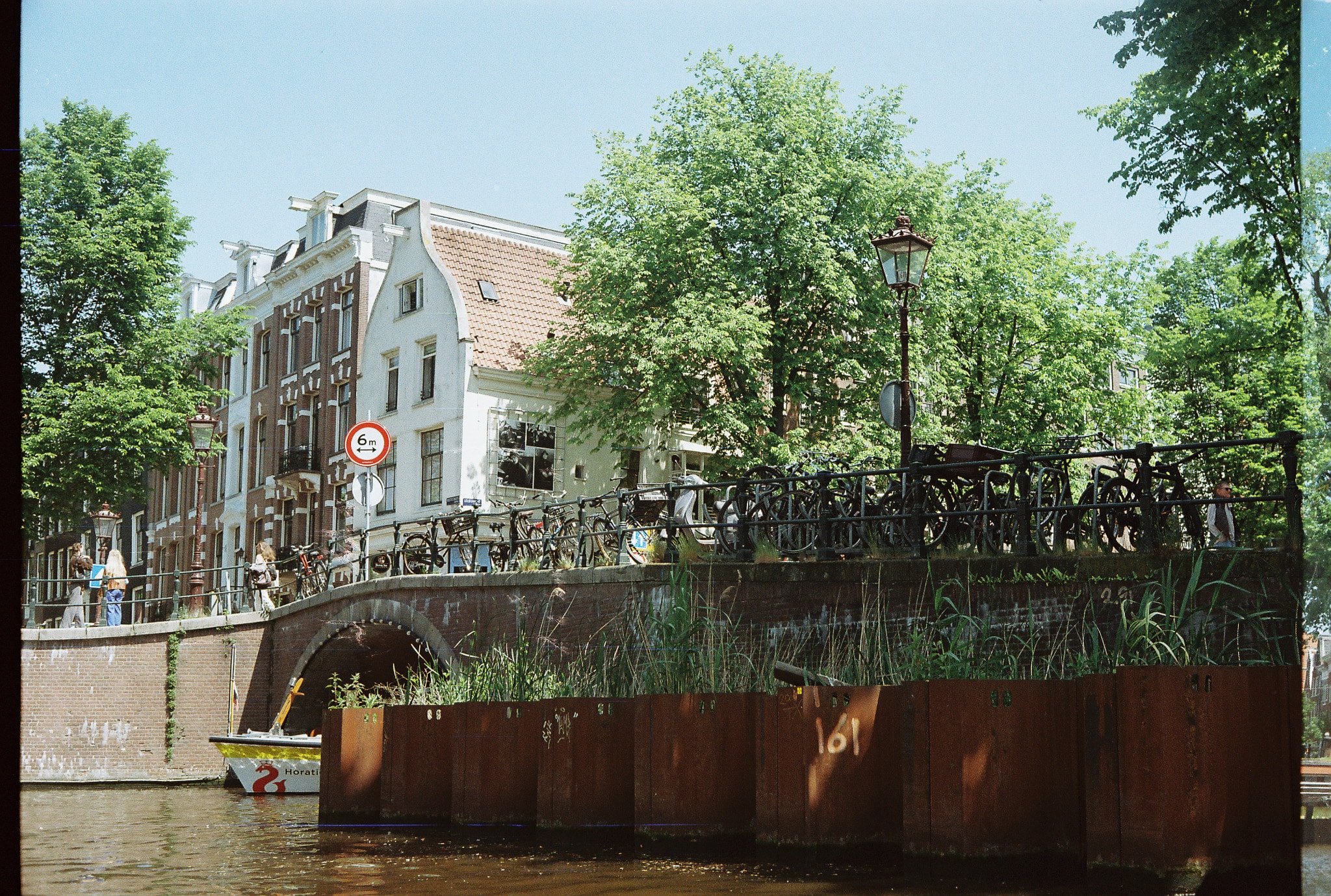 Amsterdam canal bridge lined with parked bicycles, railings, trees, and historic houses