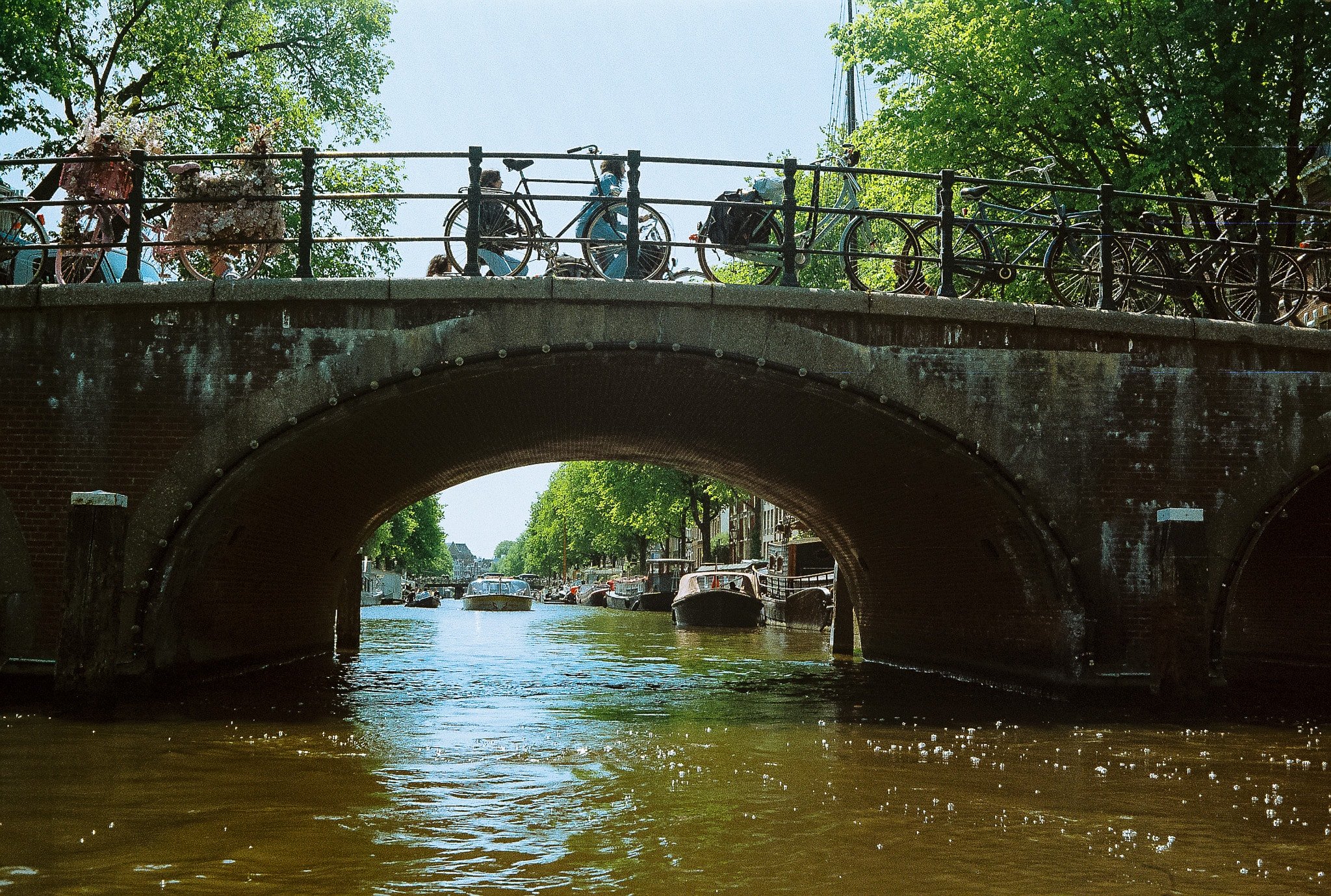 View from canal level through a brick bridge in Amsterdam with bicycles parked above and boats beyond