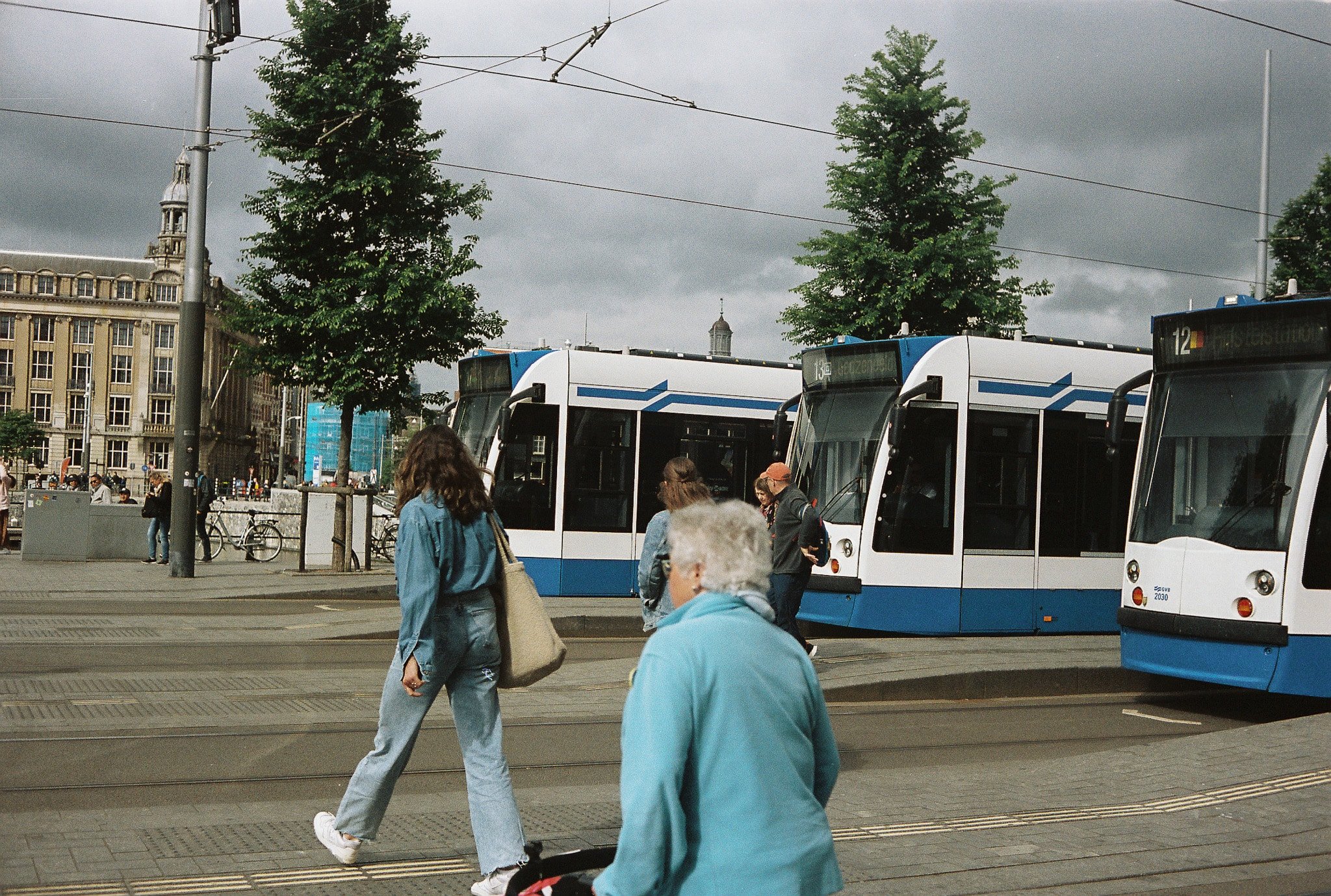 Blue and white GVB trams in central Amsterdam with overhead wires, pedestrians, and historic buildings