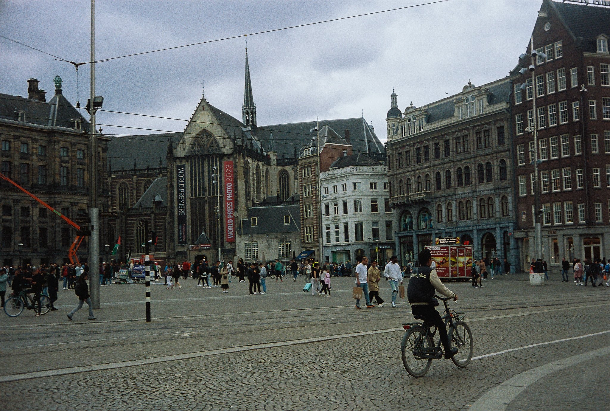 Dam Square in Amsterdam with World Press Photo banners, tram tracks, cyclists, pedestrians, and historic buildings