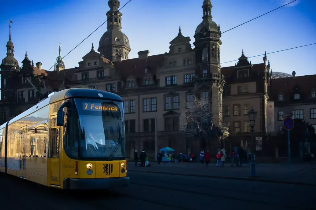 Yellow DVB tram in Dresden passing historic Baroque buildings with domed towers and overhead wires