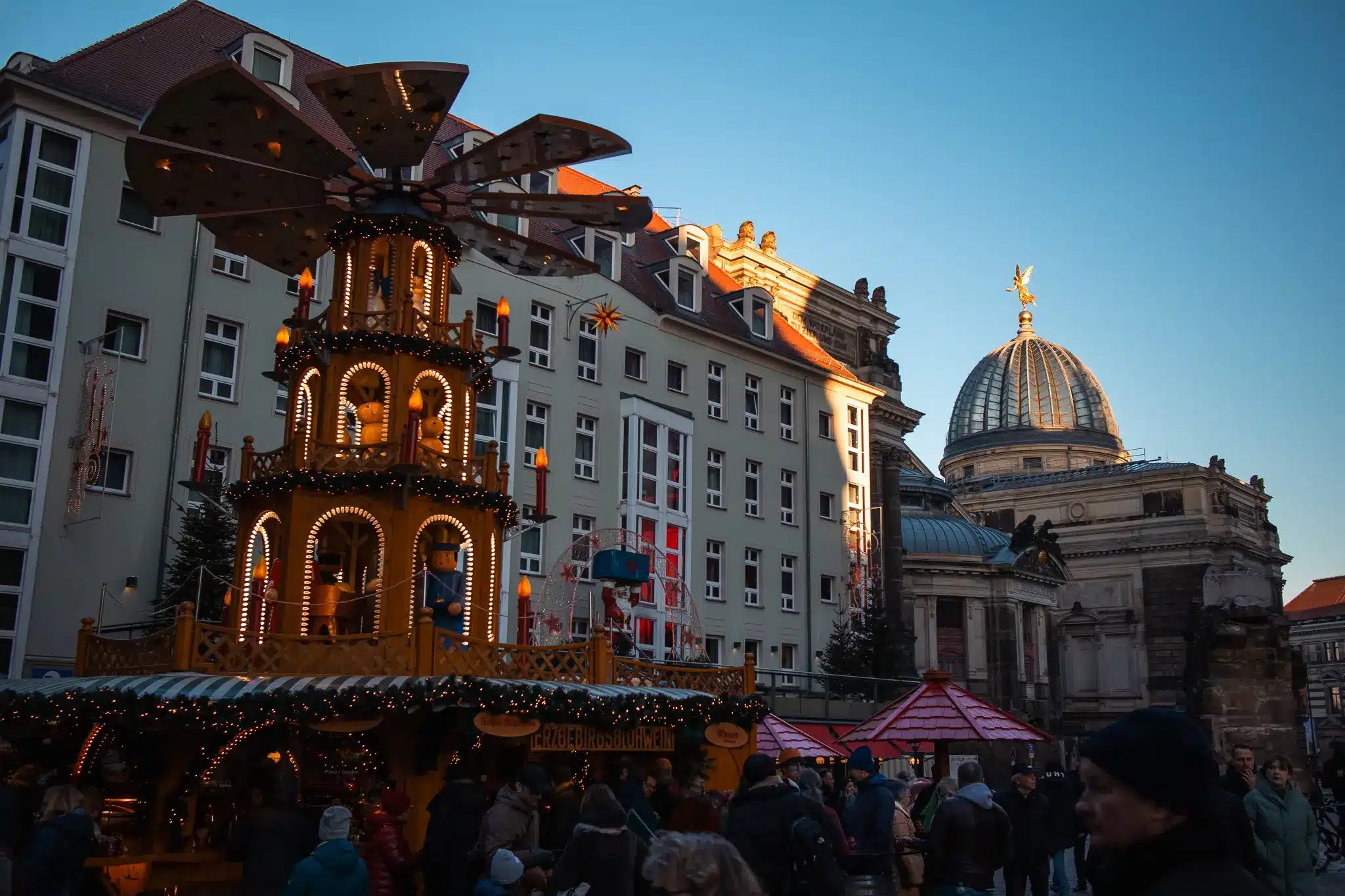 Crowded winter market scene with large wooden festive structure and historic building in Dresden