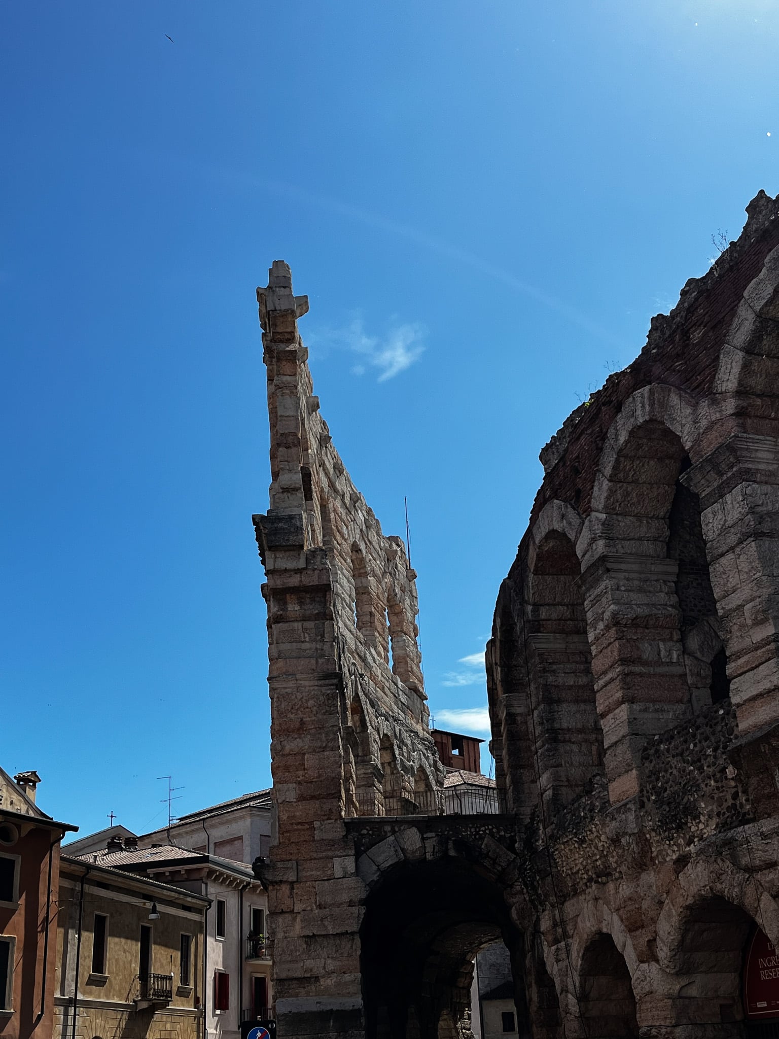 Ancient stone-and-brick ruin in Verona integrated into a street with adjacent stucco buildings and modern signage.