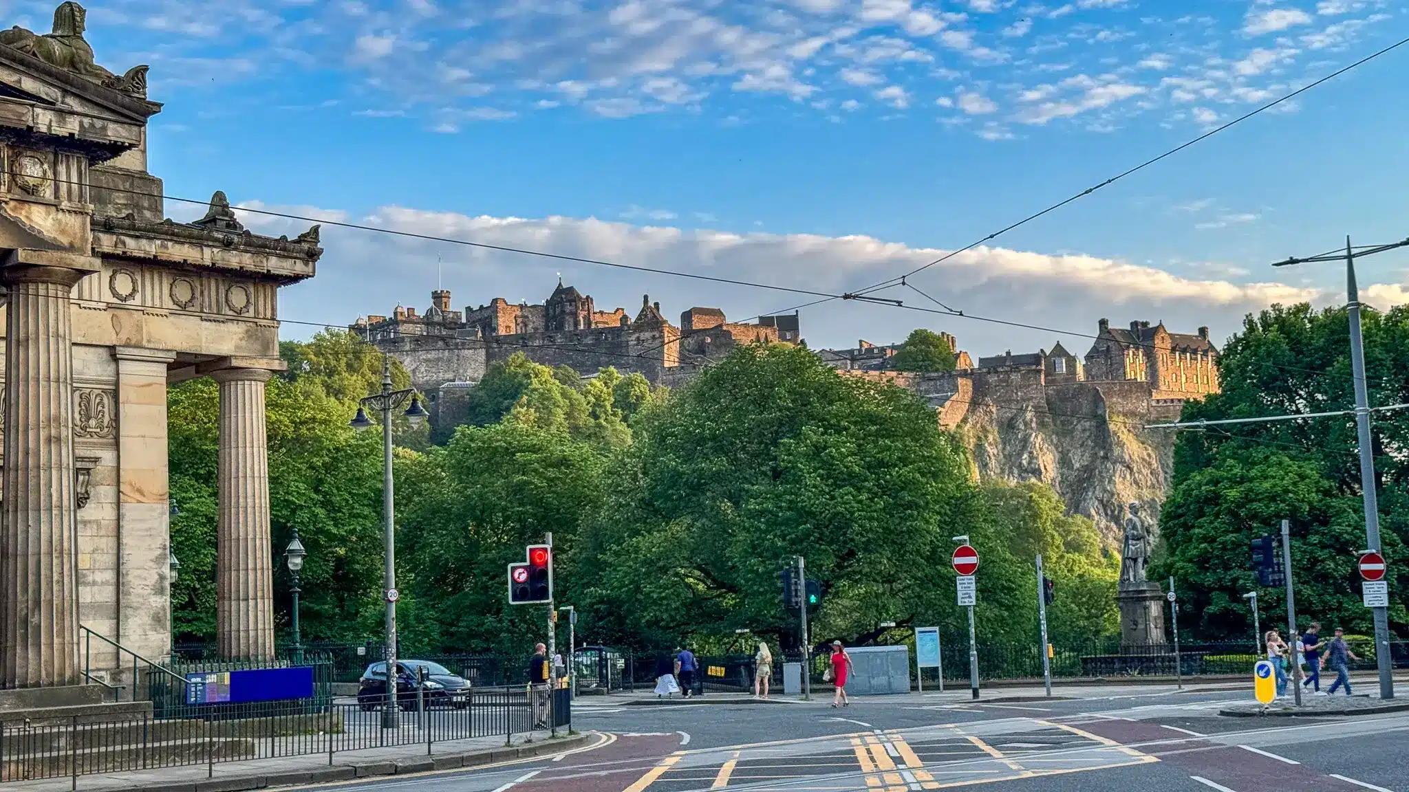 Edinburgh Castle above a city street with tram wires and traffic infrastructure