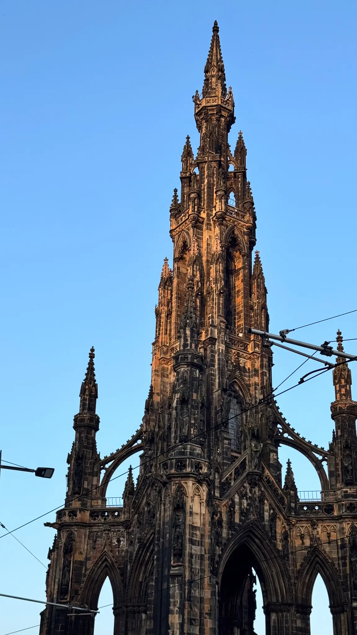 Close view of a Gothic stone spire intersected by tram wires in Edinburgh