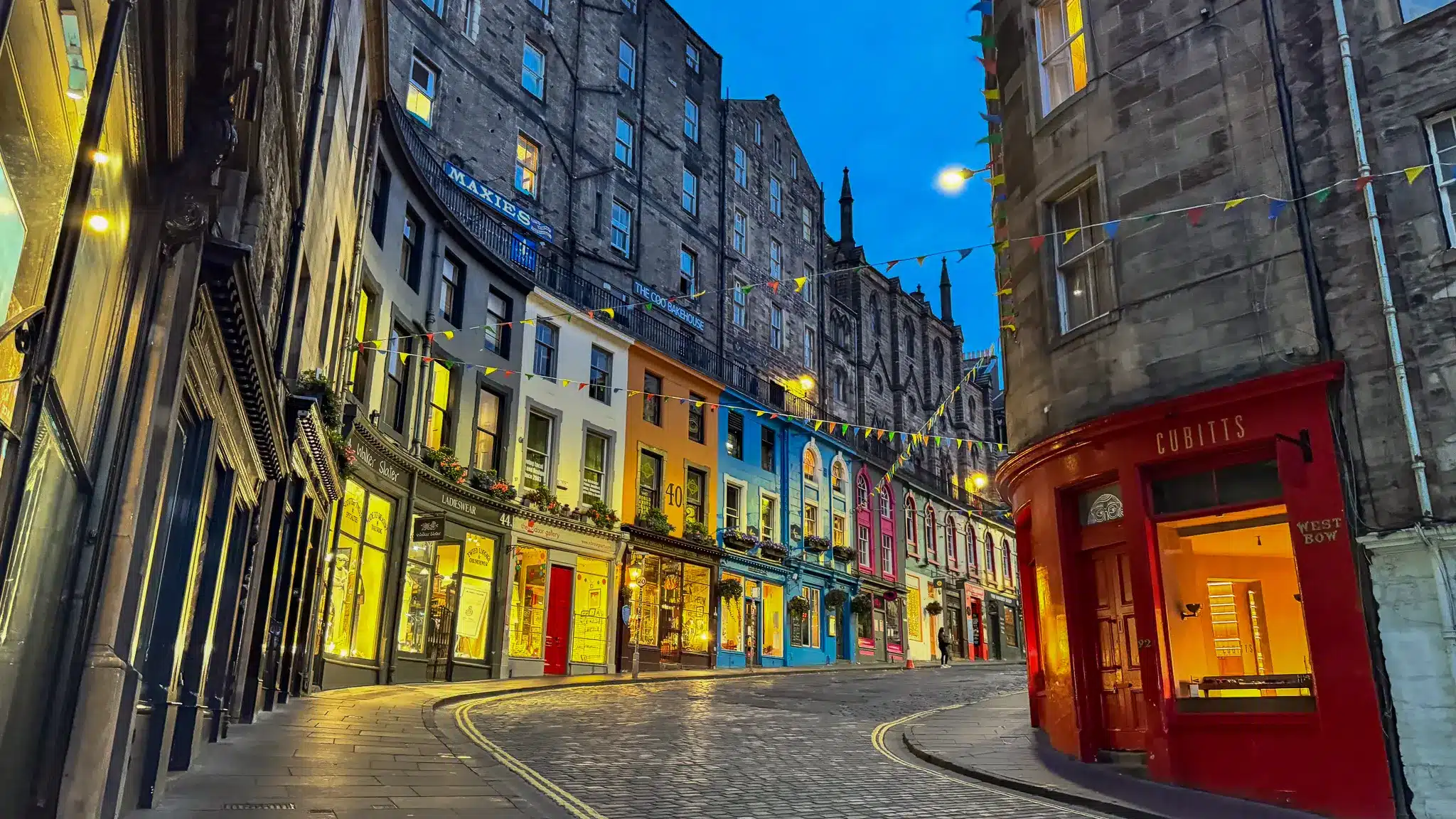 Colorful shopfronts on West Bow beneath tall stone buildings in Edinburgh