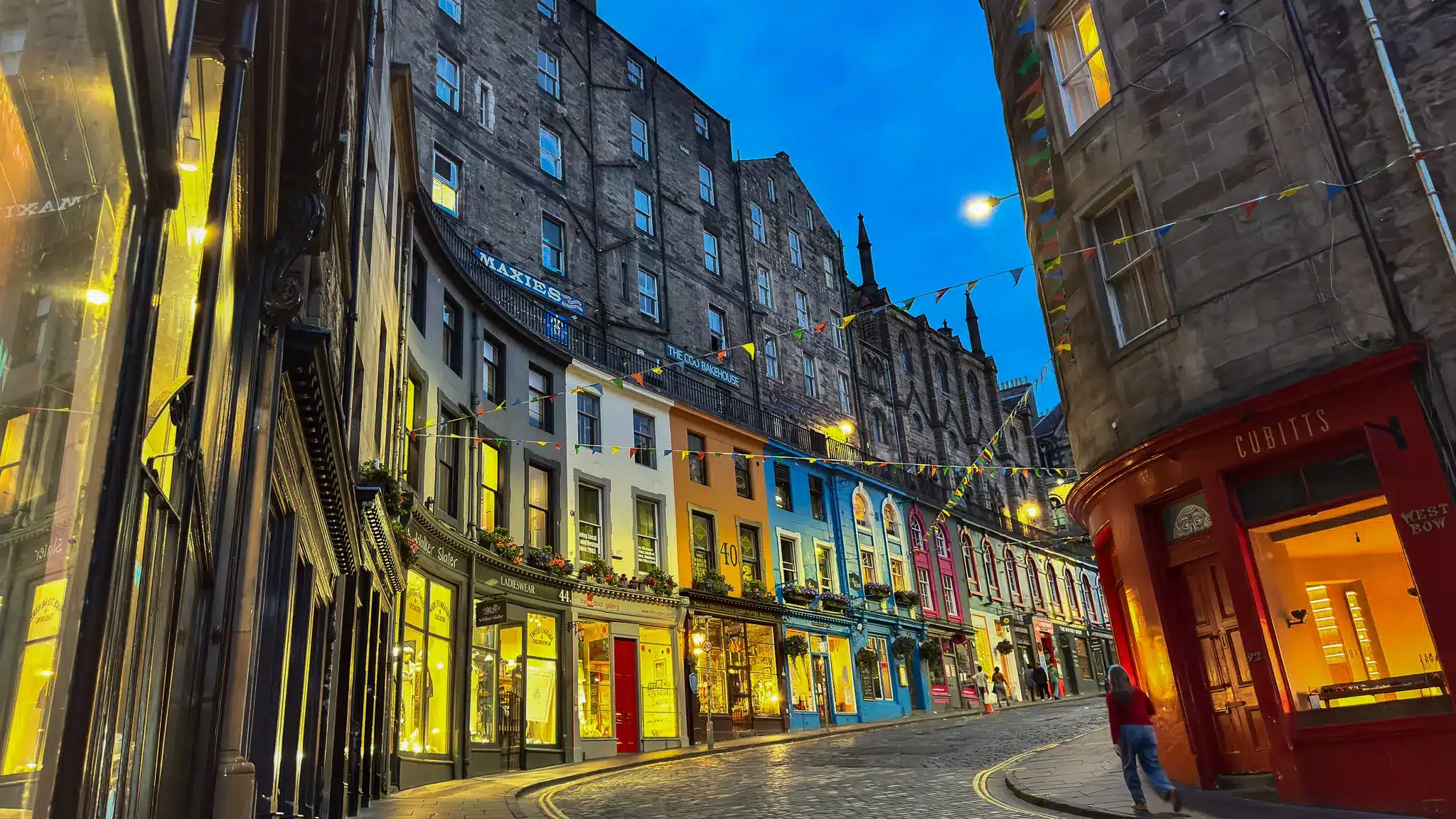 West Bow at dusk with bunting, illuminated storefronts and historic stone façades