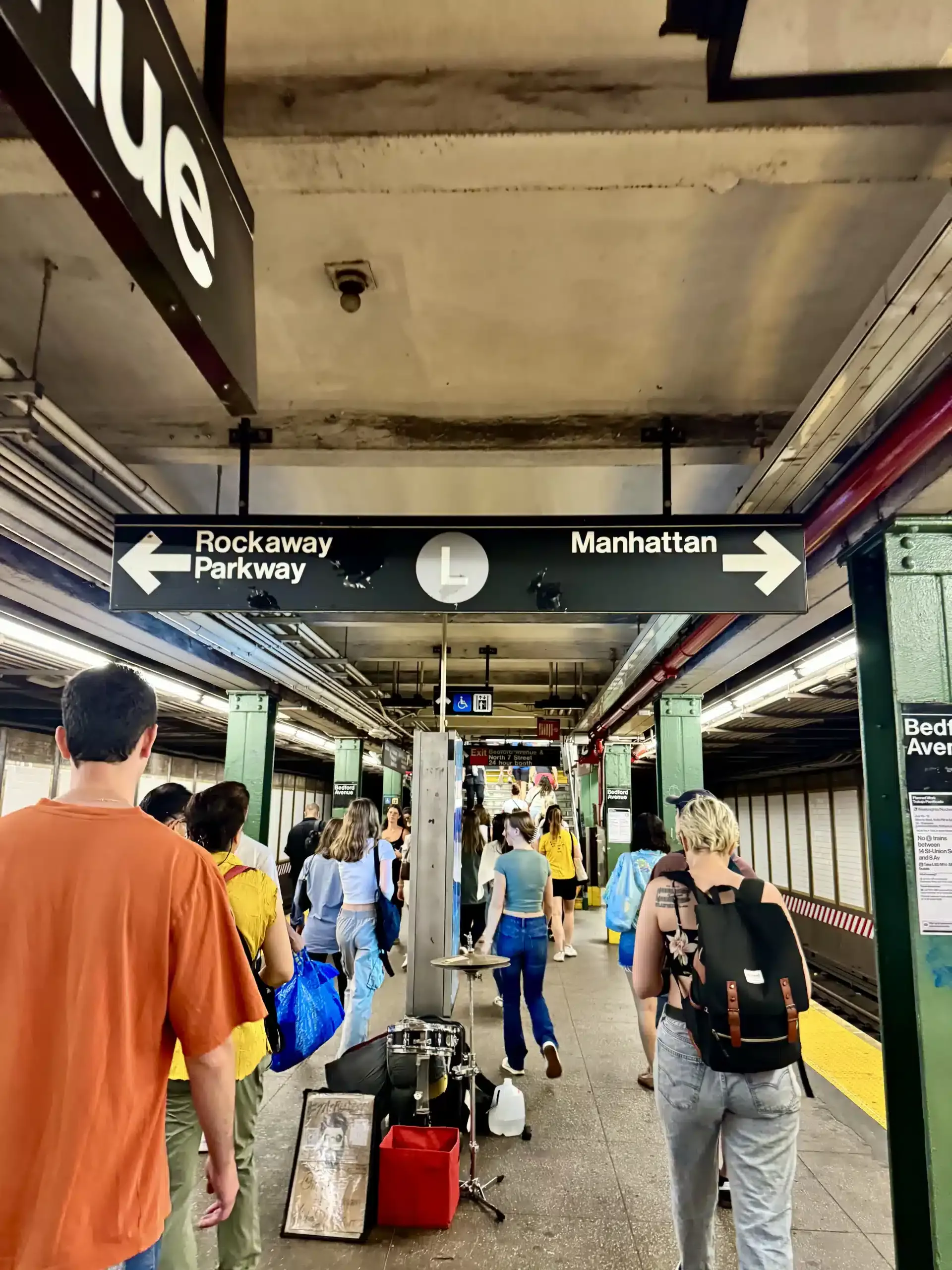 New York City subway platform with overhead sign pointing left to Rockaway Parkway and right to Manhattan on the L line.