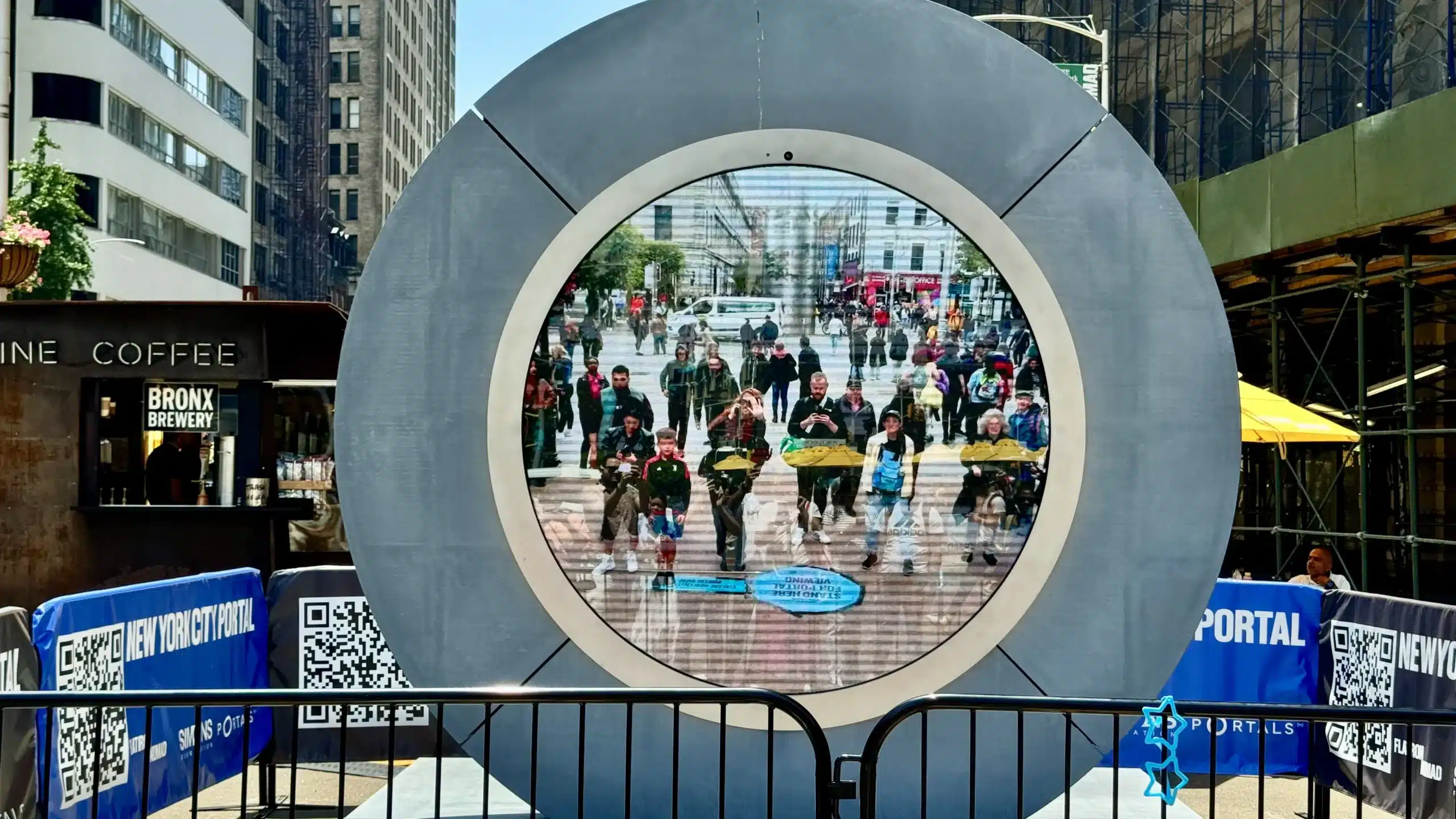 New York City Portal installation in Manhattan with circular live screen, branded fencing, QR codes, barriers, and surrounding street activity.