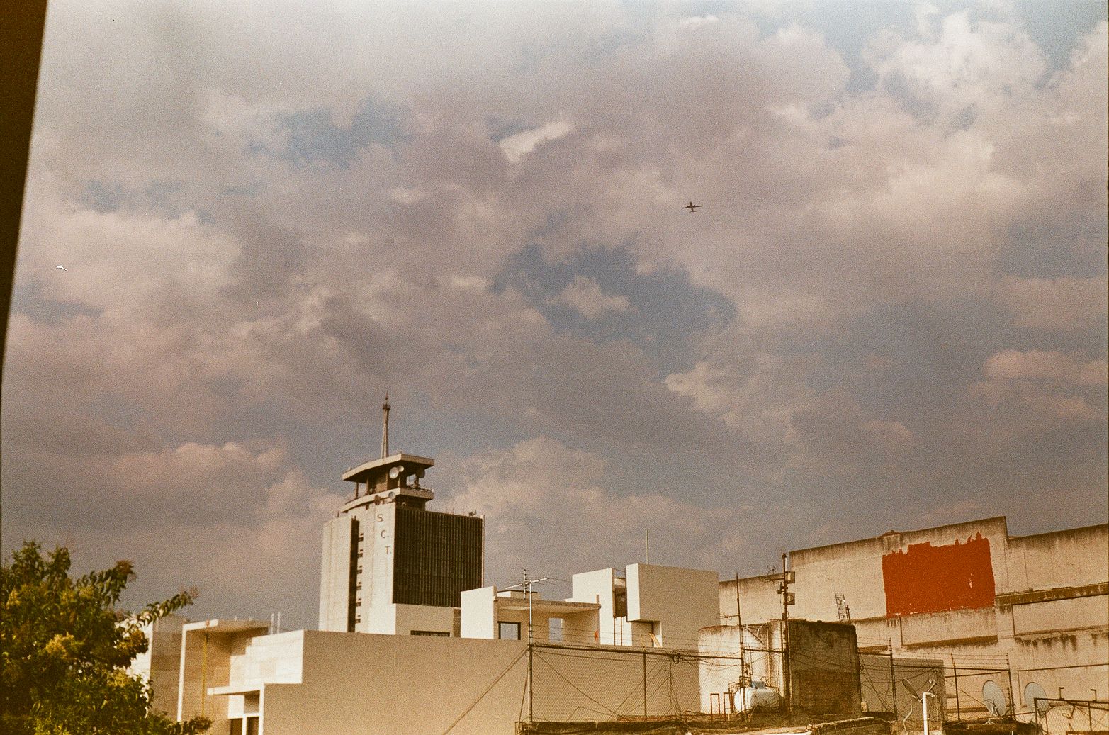 Mexico City rooftop skyline with antennas, weathered facades, and airplane in the sky