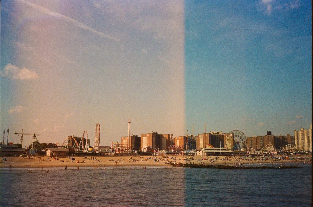 Wide view of Coney Island beach and amusement district with residential towers behind the shoreline in New York City.