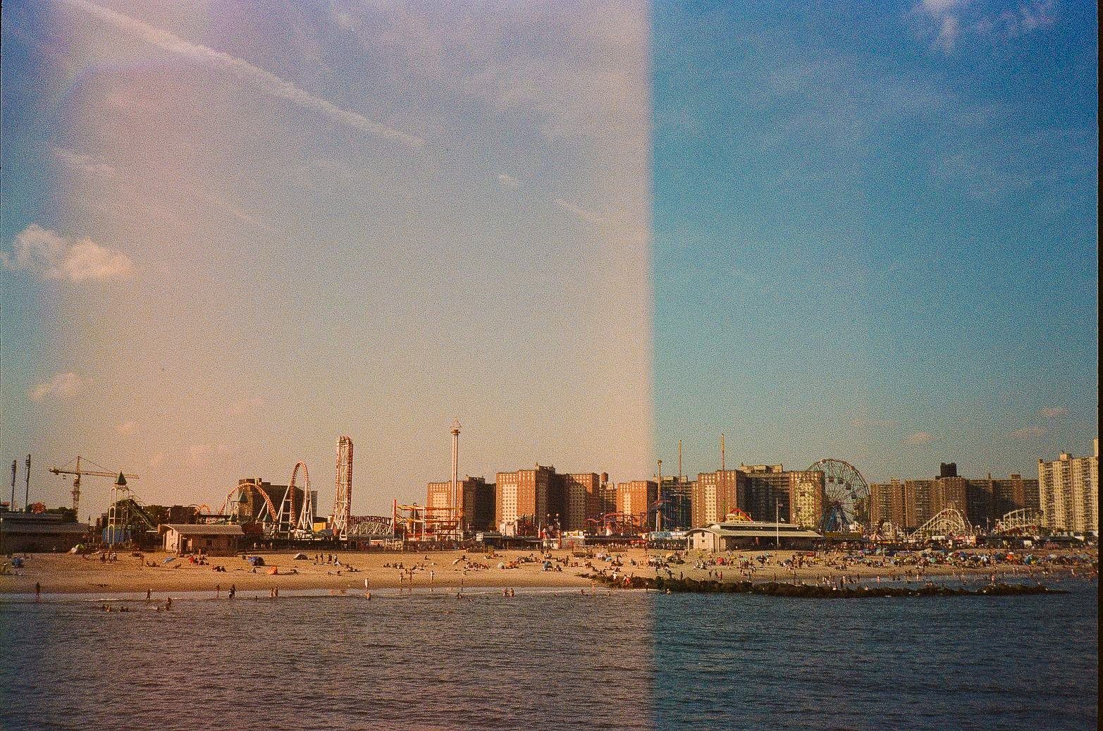 Wide view of Coney Island beach and amusement district with residential towers behind the shoreline in New York City.