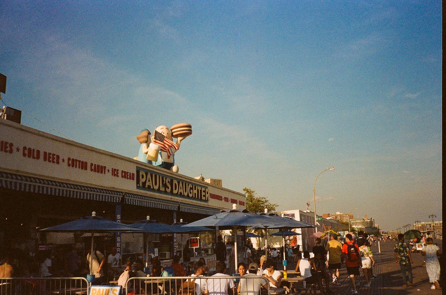 Paul's Daughter boardwalk food stand with large rooftop ice cream figures and promenade seating at Coney Island.