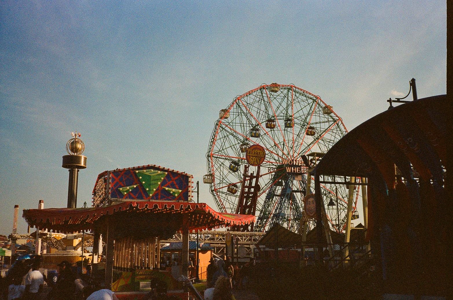 Amusement park scene with Wonder Wheel signage, Ferris wheel structure, and decorated ride facades at Coney Island.