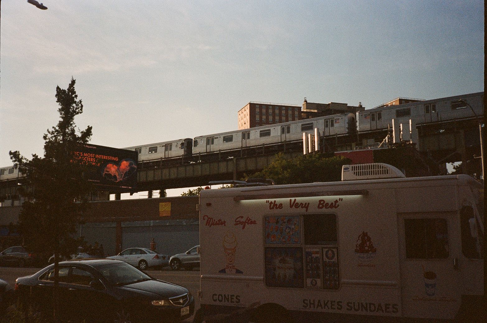 Elevated subway train passing above street traffic and an ice cream truck near Coney Island.