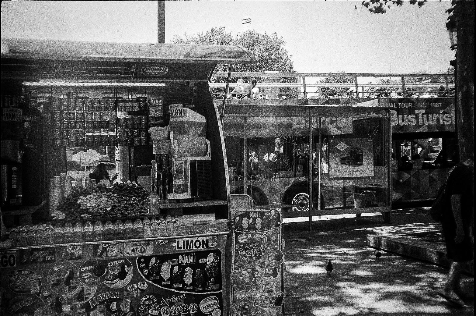 Snack kiosk with ice cream branding and an open-top sightseeing bus behind it in Barcelona