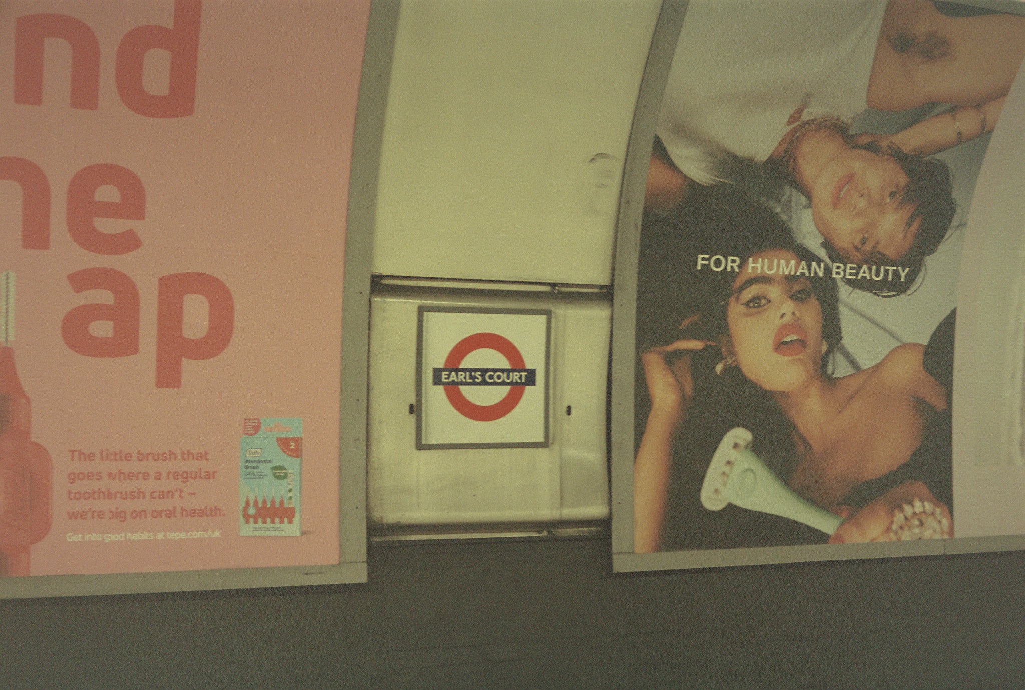 Earl's Court station sign on a London Underground wall between advertising posters.
