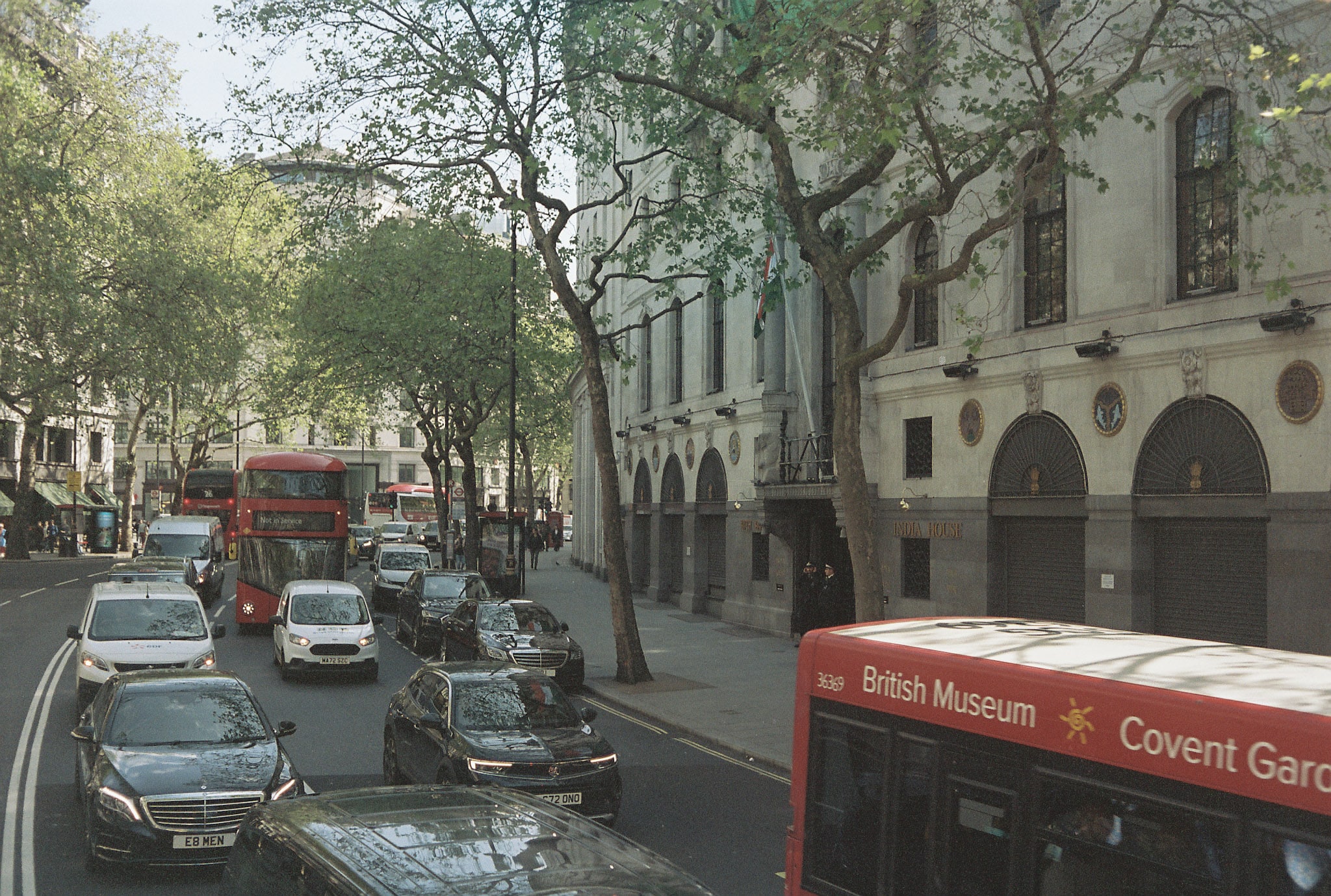 Central London street by India House with red buses and route display text including British Museum and Covent Garden.