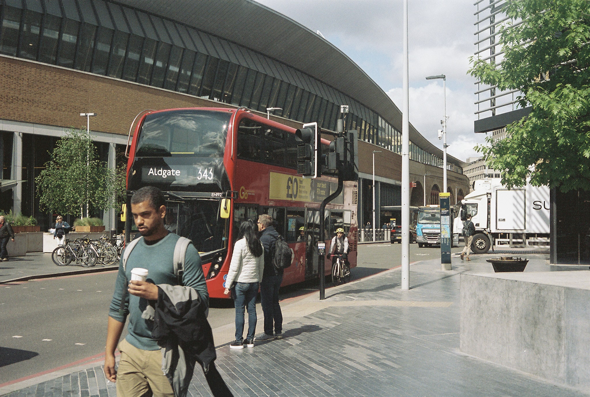Red double-decker bus showing route 343 to Aldgate with pedestrians, cyclist and modern buildings in central London.