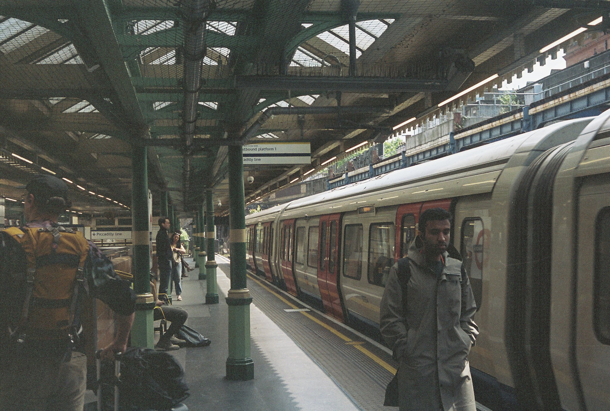 London Underground platform with green cast-iron columns, commuters waiting and a sign for Piccadilly line eastbound platform 1.