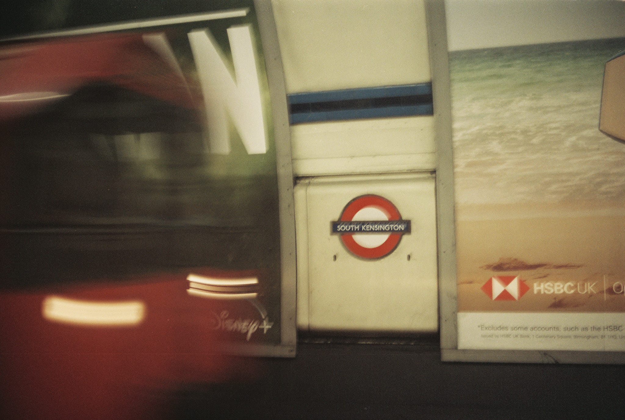 South Kensington Underground roundel inside a station with motion blur and an HSBC UK advertisement nearby.