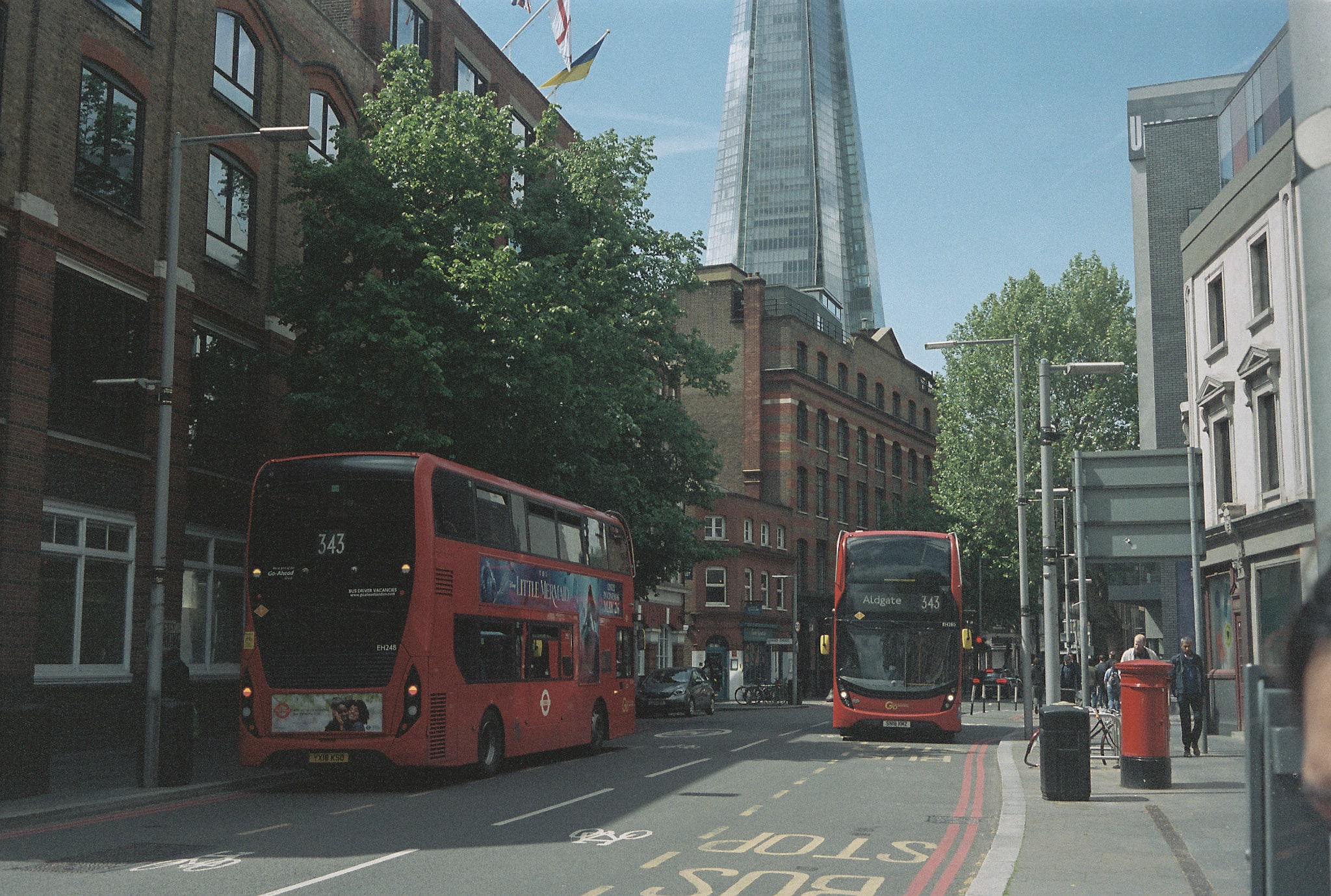 Central London street with red buses, bus stop road marking, older buildings and The Shard in the background.