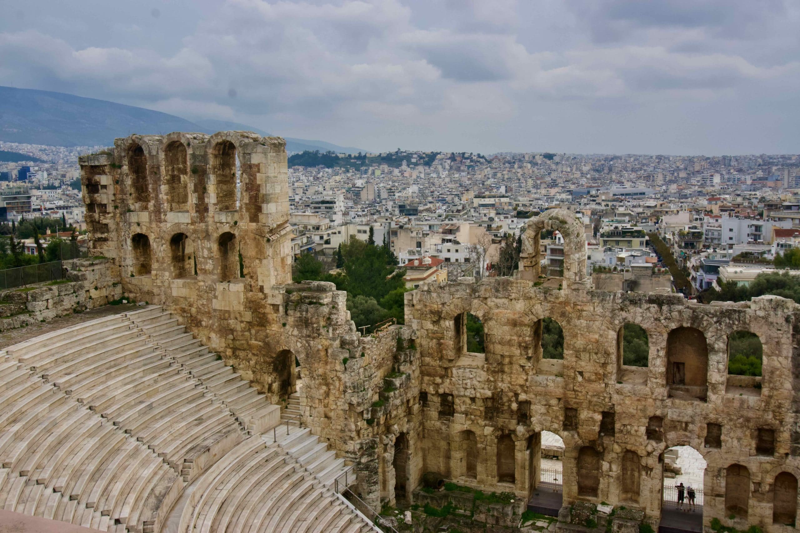 Stone amphitheater seating and arches with Athens skyline in the background