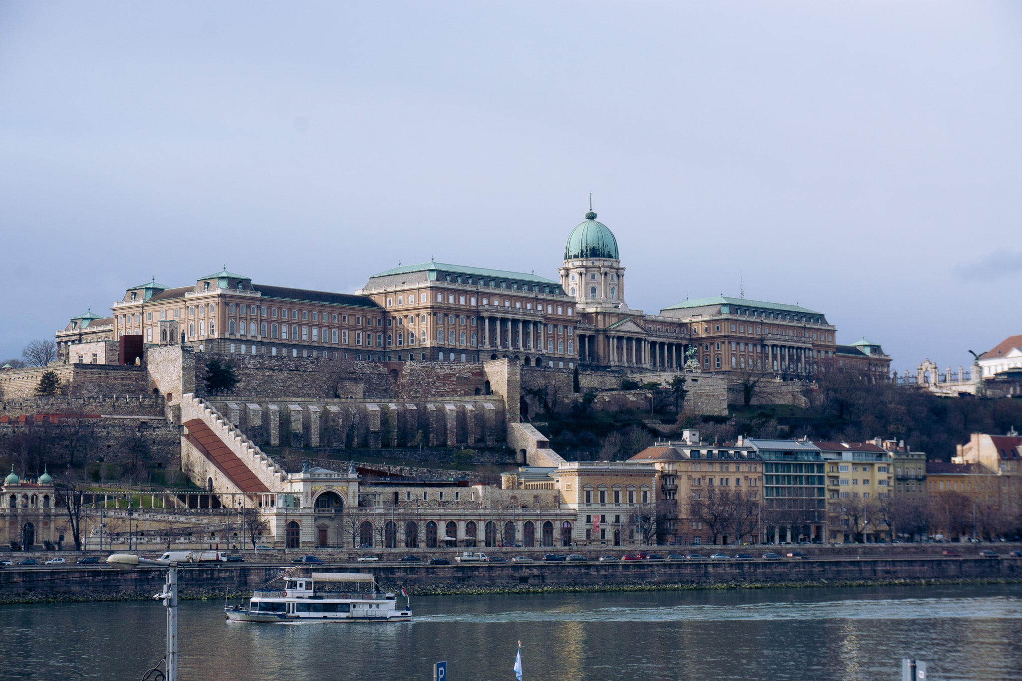 Buda Castle on the hill above the Danube with terraced fortifications and a boat on the river