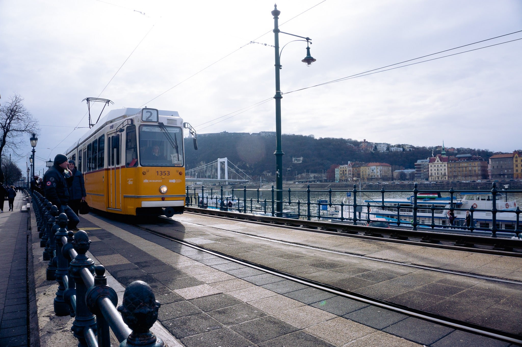 Yellow tram beside Budapest riverside promenade with bridge in the background