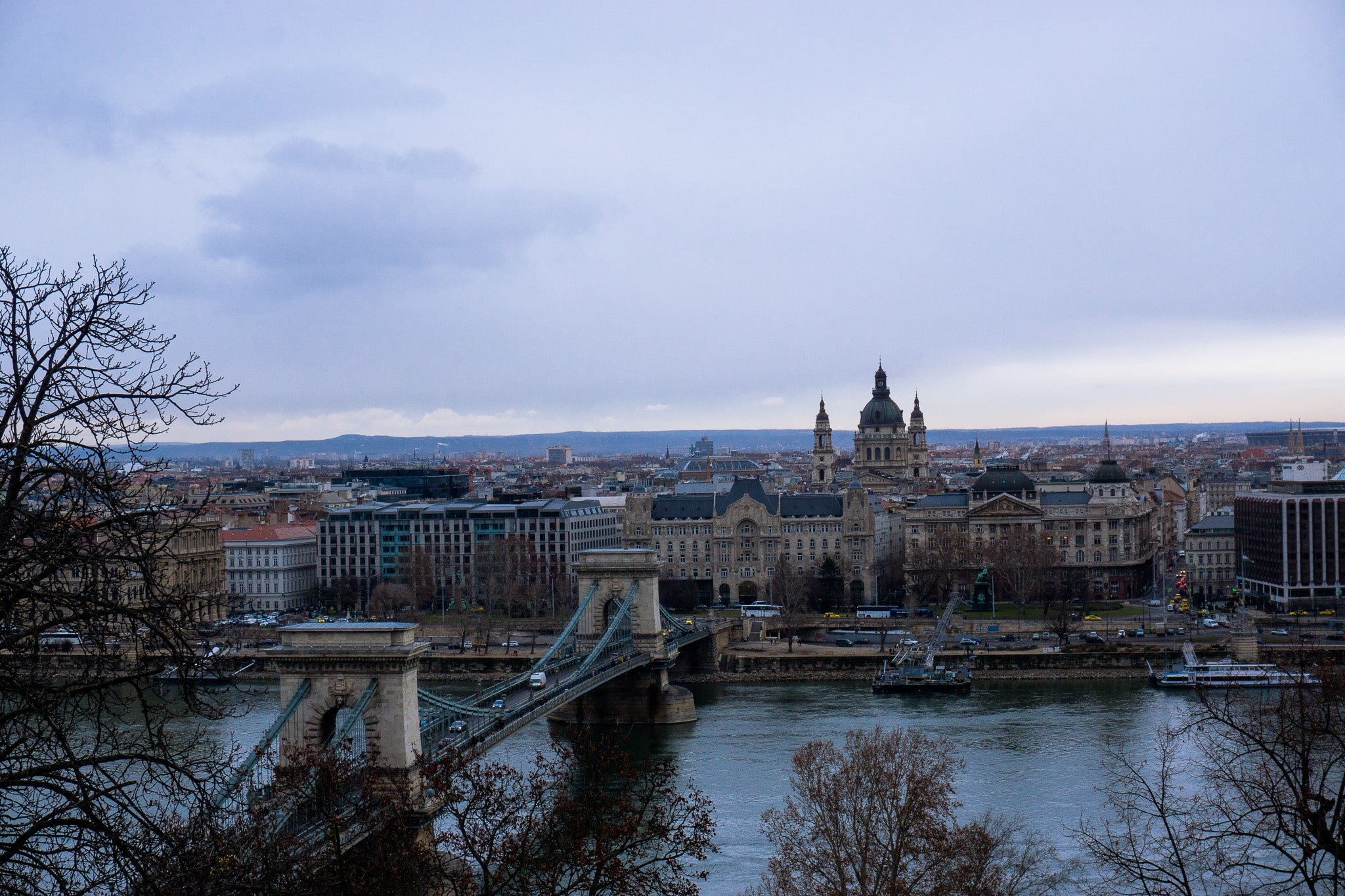 Budapest skyline with the Chain Bridge, riverside road traffic, and St. Stephen Basilica under cloudy skies