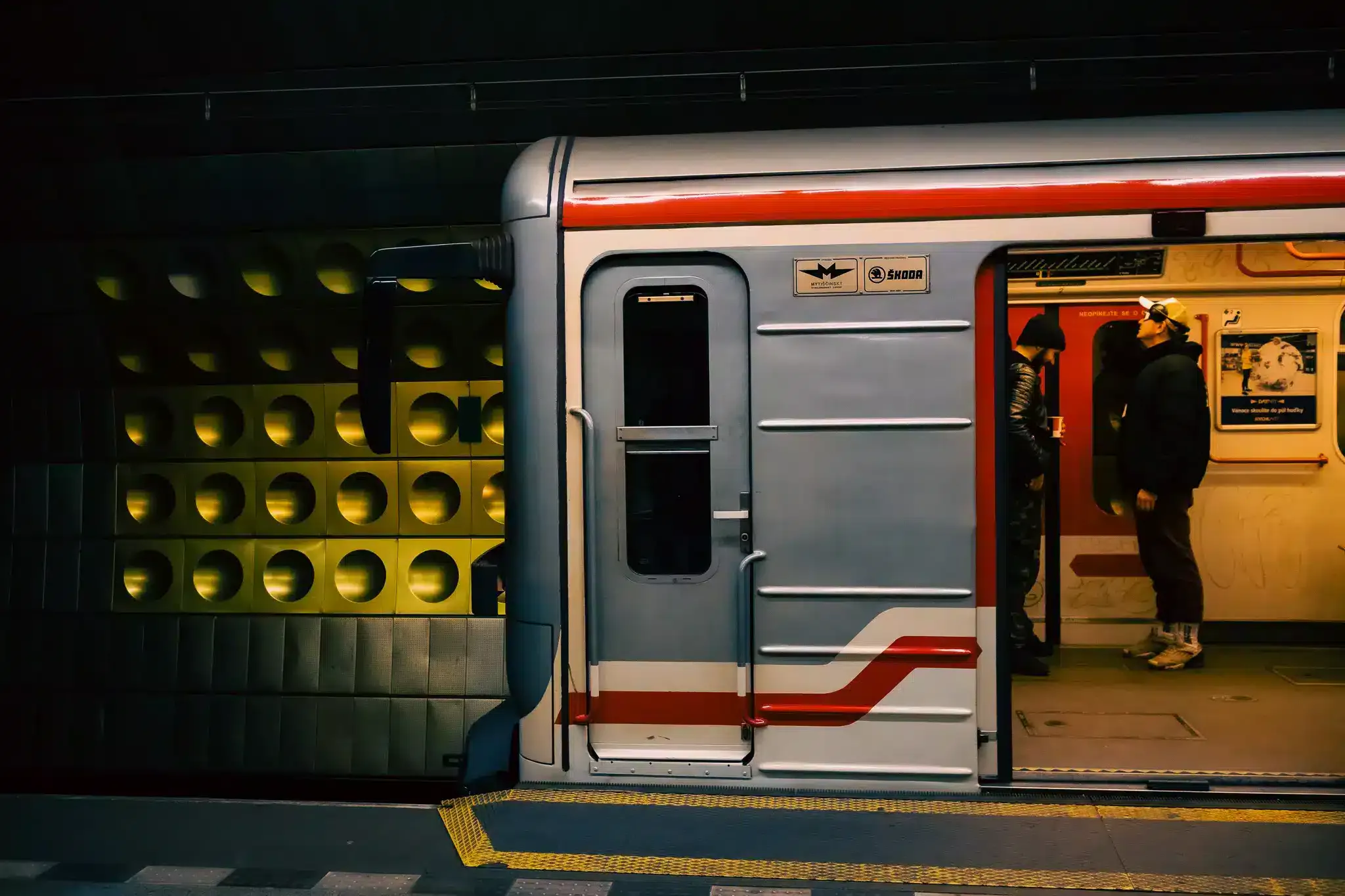 Prague metro train at an underground platform with red and grey livery and tactile paving.