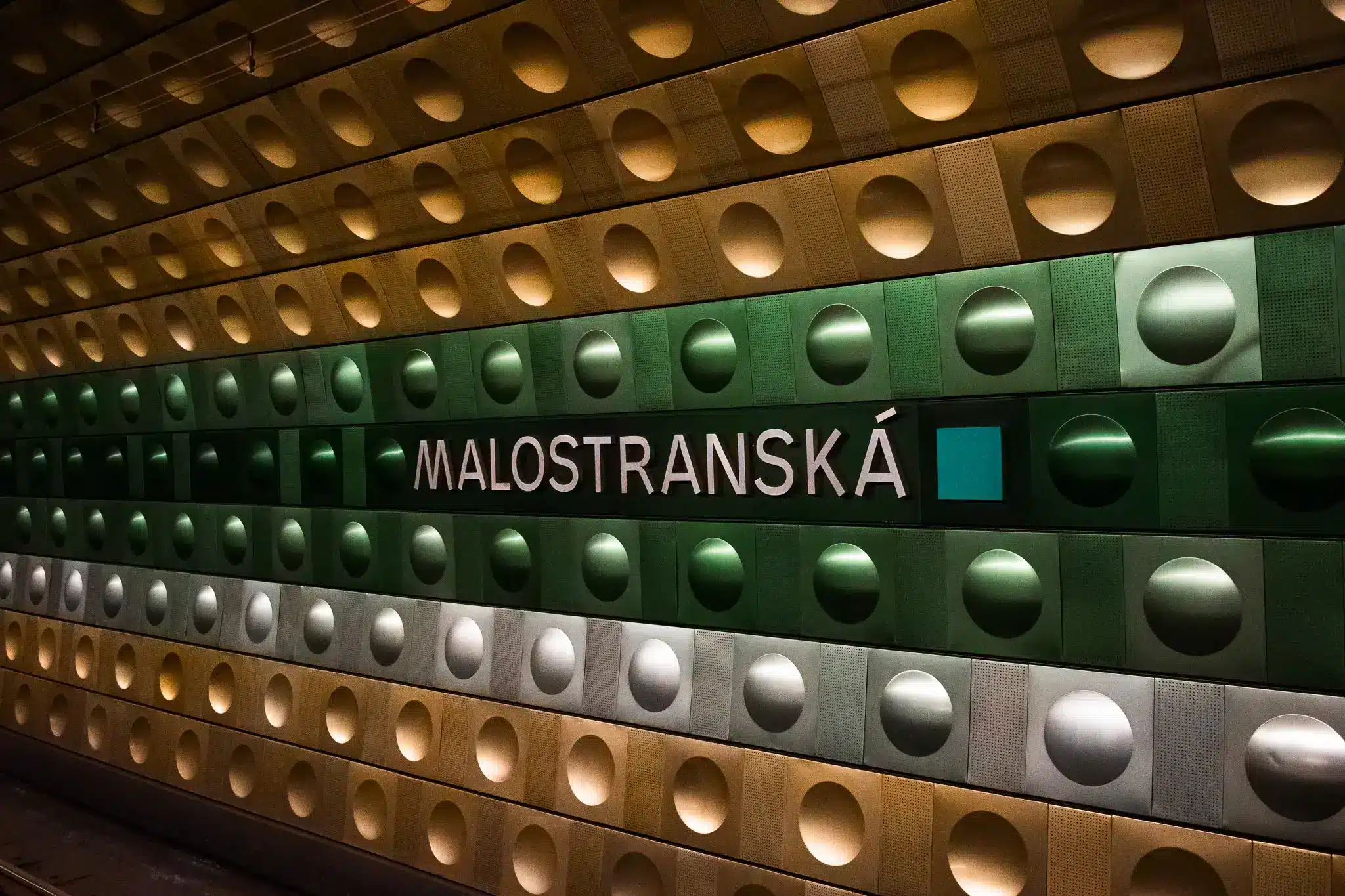Malostranská metro station wall in Prague with repeating circular metallic panels and station name signage.