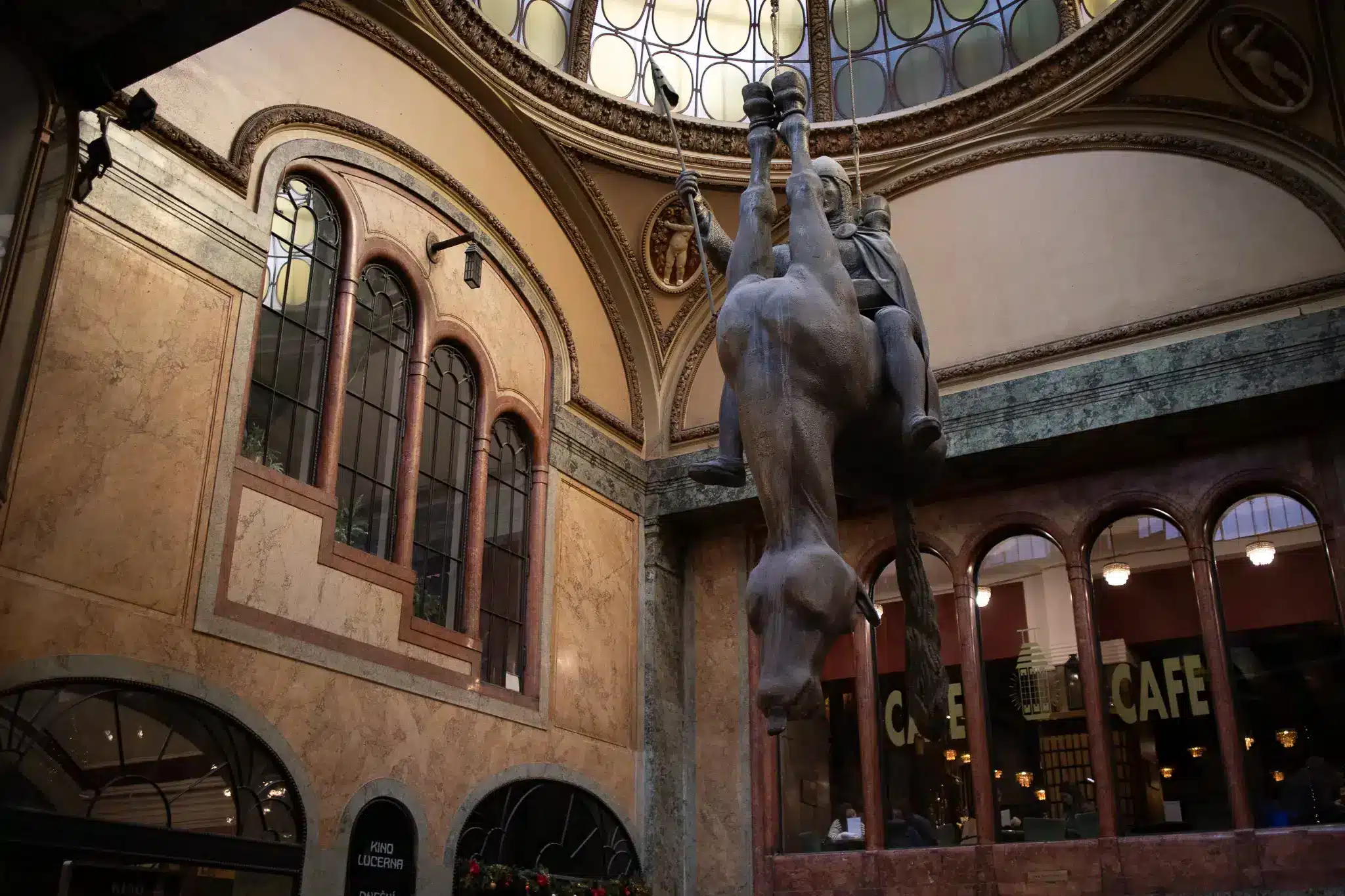 Interior of Lucerna Palace in Prague with domed skylight, Kino Lucerna sign, and upside-down horse sculpture.
