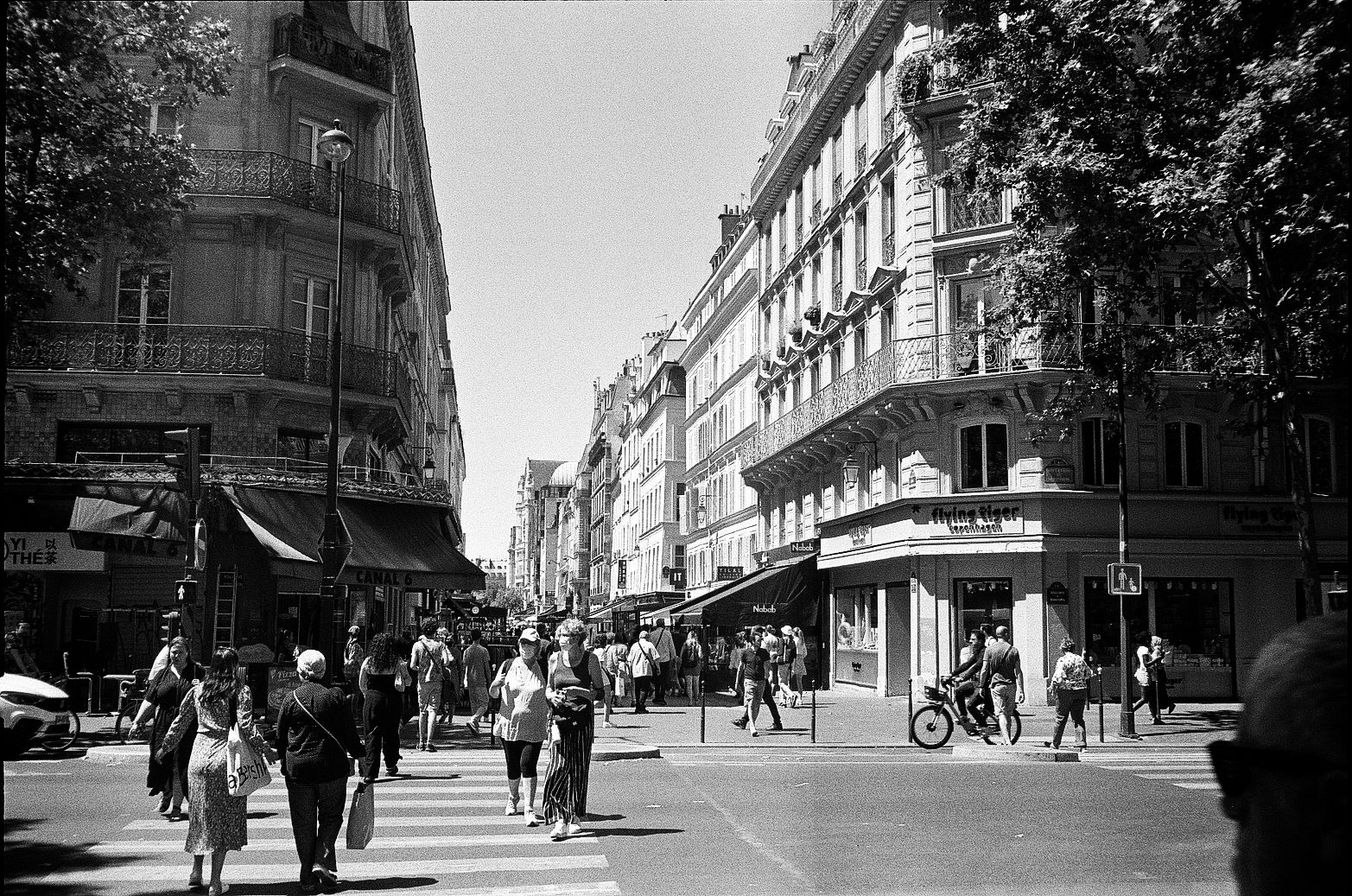 Pedestrians crossing a zebra crossing at a Paris intersection with Haussmann buildings and shopfronts