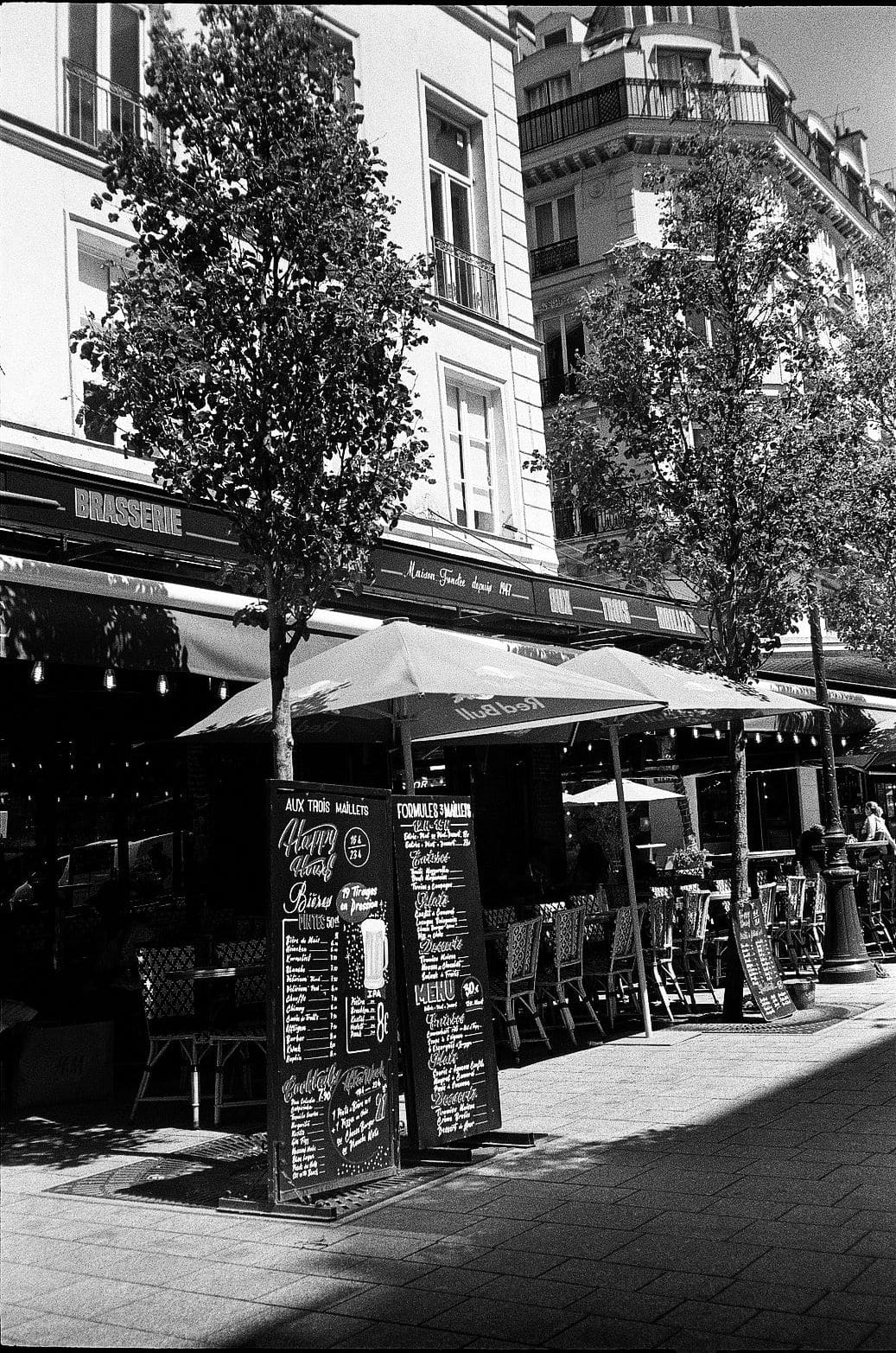 Paris brasserie frontage with outdoor terrace seating and menu boards