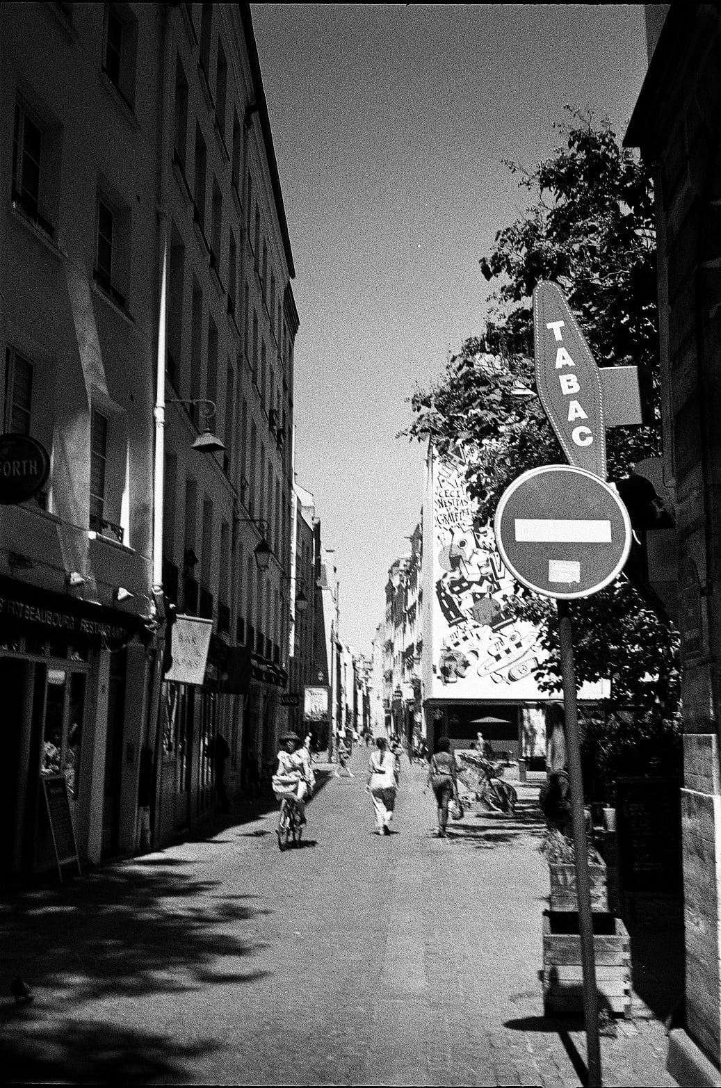 Narrow Paris street with a vertical TABAC sign and pedestrians